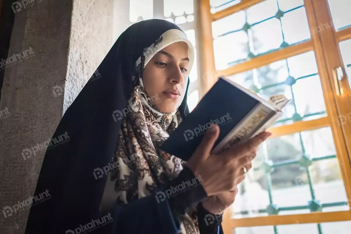 Free Premium Stock Photos Standing near a window, with natural light illuminating the scene | Muslim Woman Reading The Holy Book In A Mosque